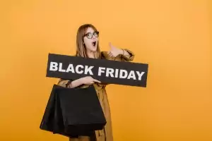 Lächelnde Frau mit Brille, Black Friday-Schild und Papiertüten vor gelbem Hintergrund Lächelnde Frau mit Brille, Black Friday-Schild und Papiertüten vor gelbem Hintergrund